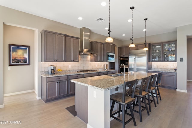 kitchen featuring a breakfast bar, a kitchen island with sink, sink, built in appliances, and wall chimney exhaust hood