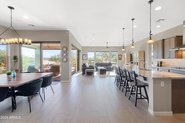 kitchen featuring a kitchen breakfast bar, light stone counters, backsplash, decorative light fixtures, and ceiling fan with notable chandelier