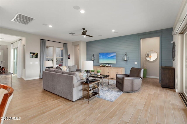 living room with light wood-type flooring, ceiling fan, and wooden walls