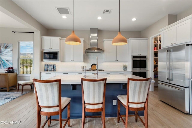 kitchen featuring appliances with stainless steel finishes, wall chimney exhaust hood, white cabinets, and hanging light fixtures