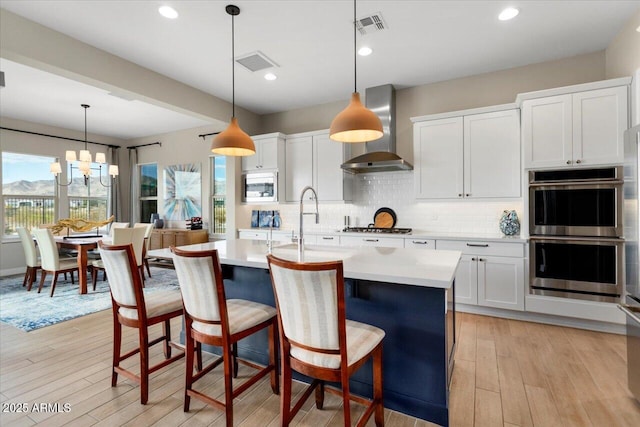 kitchen featuring stainless steel appliances, wall chimney exhaust hood, white cabinets, and pendant lighting