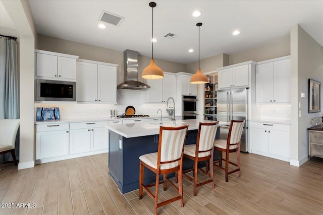 kitchen featuring decorative light fixtures, wall chimney exhaust hood, white cabinets, and built in appliances