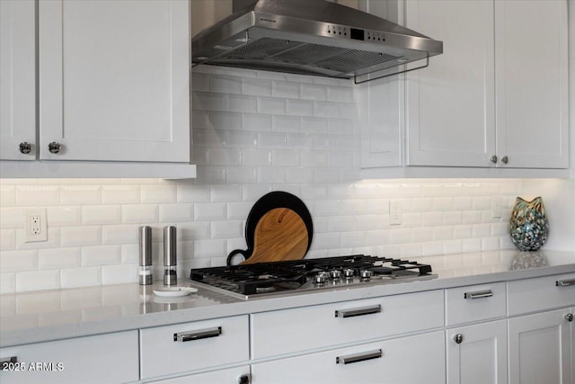 kitchen featuring exhaust hood, backsplash, stainless steel gas stovetop, light stone countertops, and white cabinets