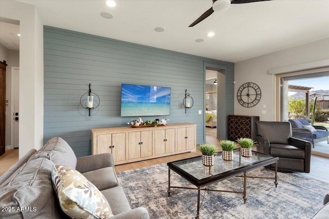 living room featuring light hardwood / wood-style floors, ceiling fan, a barn door, and wooden walls