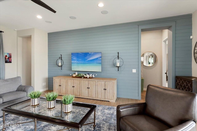 living room with light hardwood / wood-style floors, wood walls, and ceiling fan