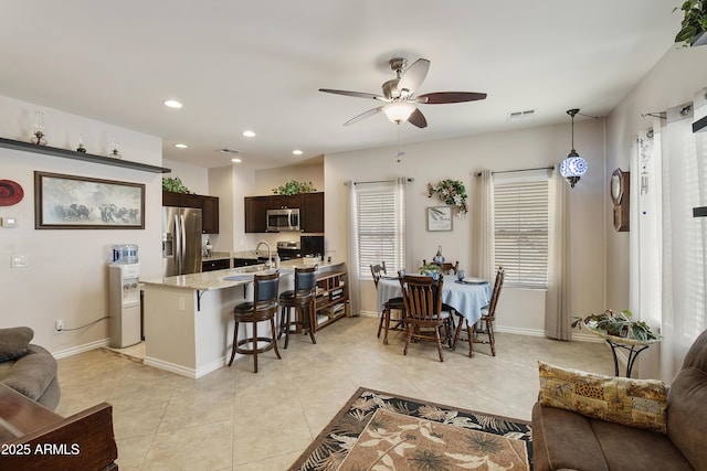 kitchen featuring a breakfast bar, appliances with stainless steel finishes, hanging light fixtures, dark brown cabinets, and light stone countertops