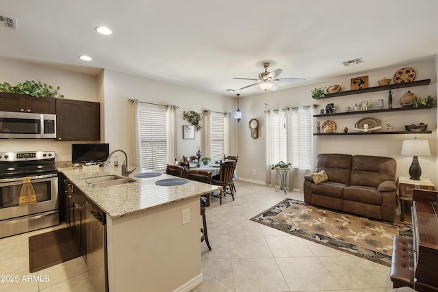 kitchen with appliances with stainless steel finishes, sink, a breakfast bar area, light tile patterned floors, and light stone countertops