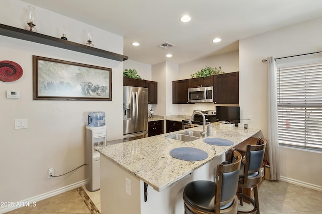 kitchen featuring a breakfast bar, sink, light tile patterned floors, appliances with stainless steel finishes, and light stone countertops