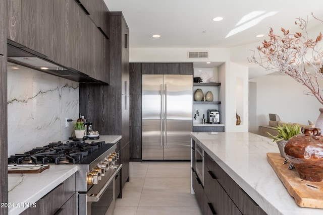 kitchen featuring dark brown cabinetry, light tile patterned floors, decorative backsplash, and premium appliances