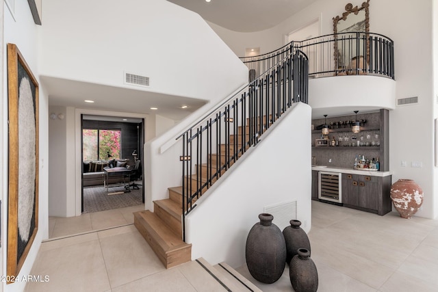 stairs featuring wine cooler, tile patterned flooring, a towering ceiling, and bar