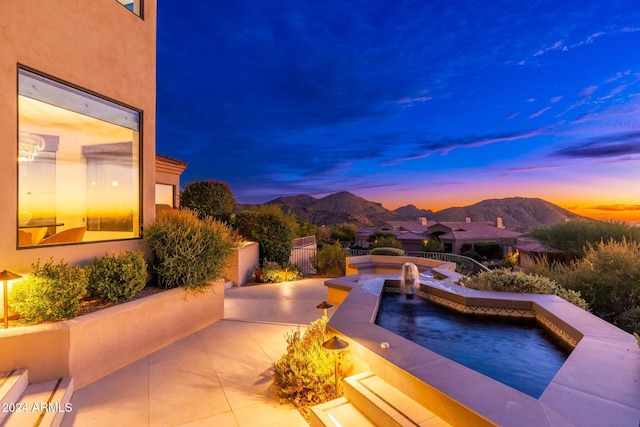 pool at dusk with a jacuzzi, a mountain view, and a patio area