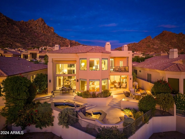 back house at dusk with a mountain view, a patio, a balcony, and an in ground hot tub