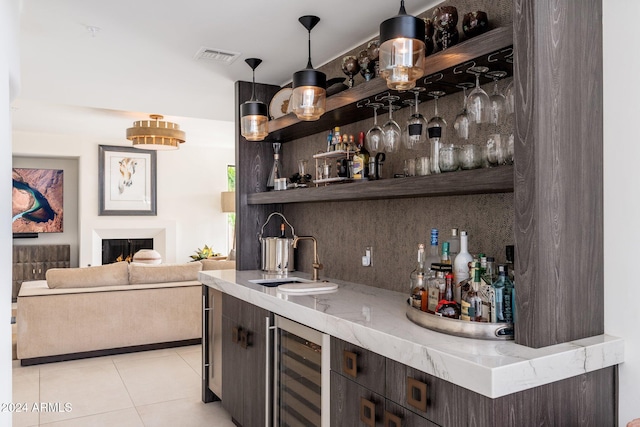 bar featuring light tile patterned flooring, decorative light fixtures, sink, wine cooler, and dark brown cabinets