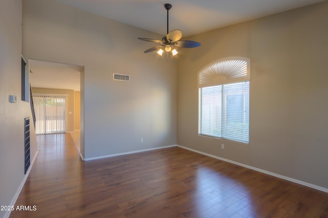 empty room featuring ceiling fan, a high ceiling, dark hardwood / wood-style floors, and a healthy amount of sunlight