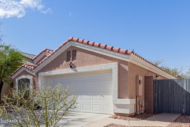 view of front of property featuring fence, a tiled roof, an attached garage, and stucco siding