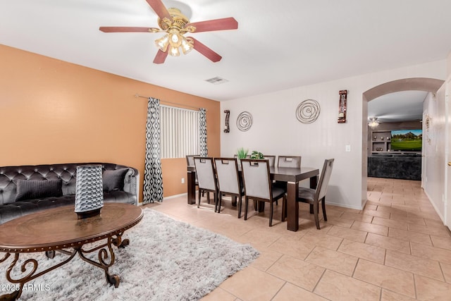 dining area with light tile patterned floors, baseboards, visible vents, arched walkways, and a ceiling fan