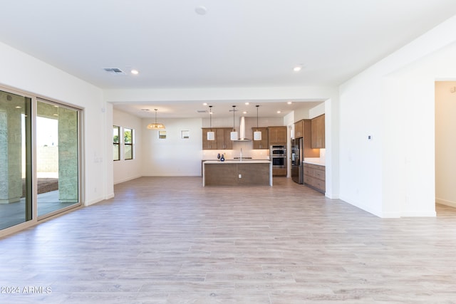 kitchen featuring light hardwood / wood-style floors, an island with sink, stainless steel appliances, wall chimney exhaust hood, and pendant lighting