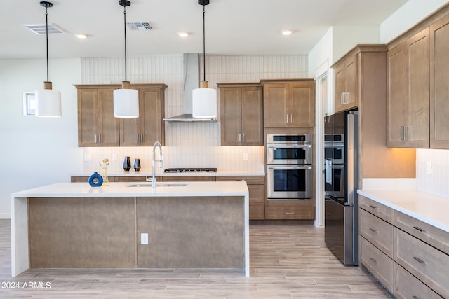 kitchen with decorative light fixtures, appliances with stainless steel finishes, sink, wall chimney range hood, and tasteful backsplash