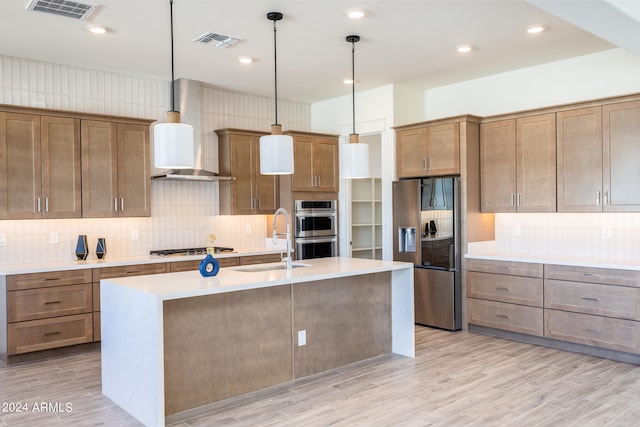 kitchen featuring an island with sink, tasteful backsplash, appliances with stainless steel finishes, and wall chimney range hood