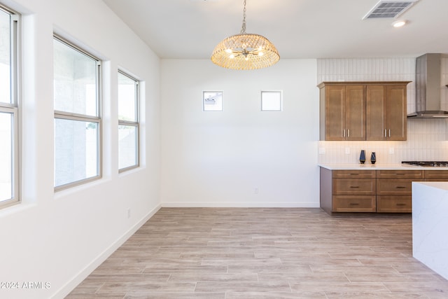 kitchen with pendant lighting, a notable chandelier, wall chimney range hood, gas cooktop, and backsplash