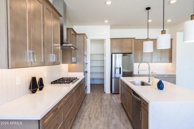 kitchen featuring an island with sink, pendant lighting, appliances with stainless steel finishes, light hardwood / wood-style floors, and tasteful backsplash