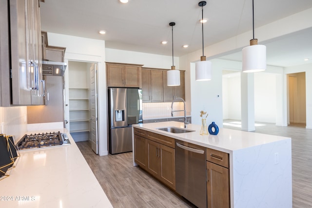 kitchen with sink, an island with sink, stainless steel appliances, tasteful backsplash, and pendant lighting