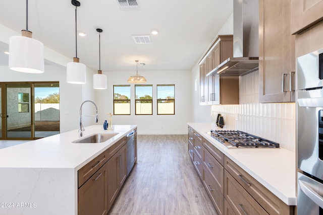 kitchen featuring tasteful backsplash, a kitchen island with sink, pendant lighting, wall chimney range hood, and sink