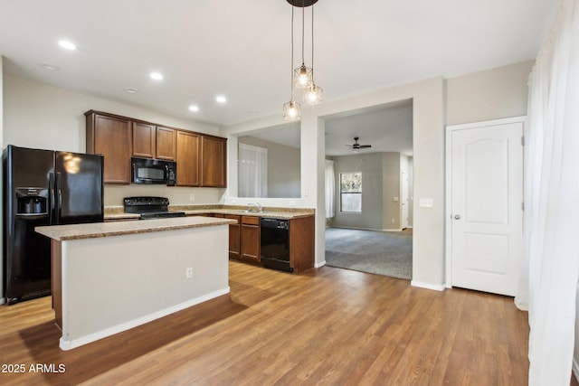 kitchen with sink, decorative light fixtures, light hardwood / wood-style flooring, a kitchen island, and black appliances