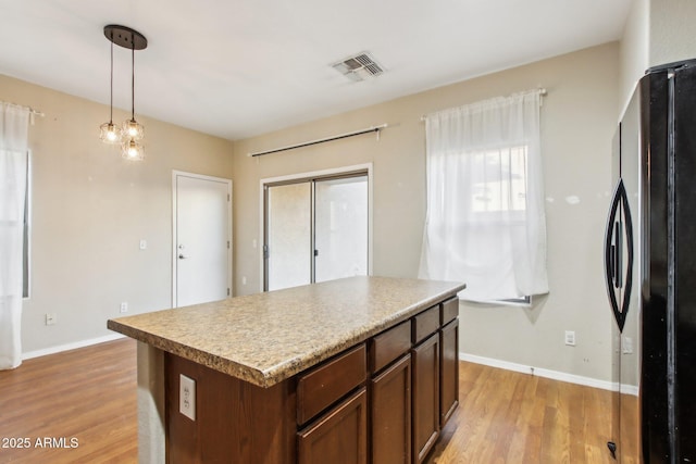 kitchen with a kitchen island, black refrigerator, pendant lighting, and light wood-type flooring