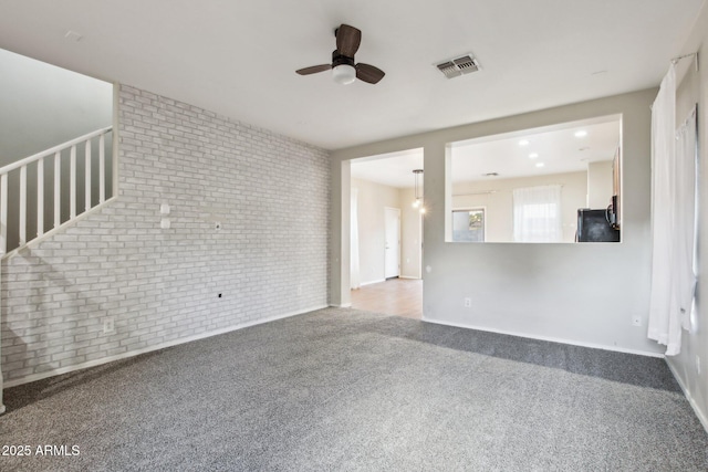 unfurnished living room with ceiling fan, brick wall, and carpet flooring