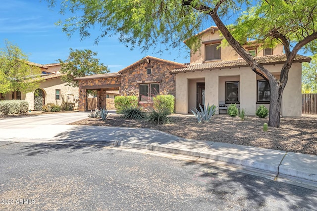 mediterranean / spanish-style home with driveway, stone siding, a tiled roof, fence, and stucco siding