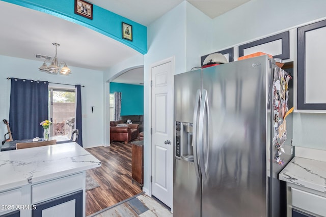 kitchen with decorative light fixtures, wood finished floors, stainless steel fridge, arched walkways, and a chandelier