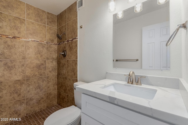 bathroom featuring vanity, toilet, and a tile shower