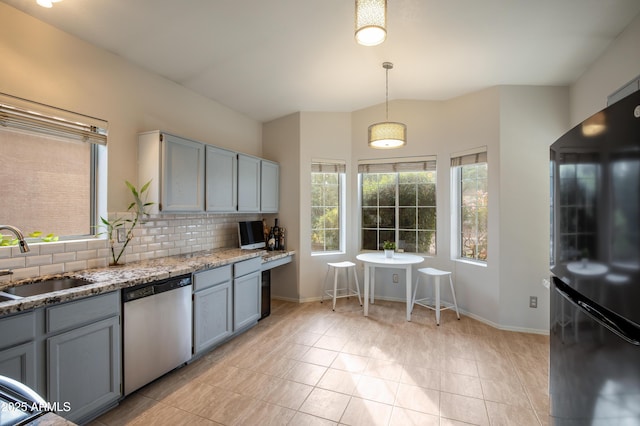 kitchen with light stone countertops, backsplash, sink, decorative light fixtures, and dishwasher