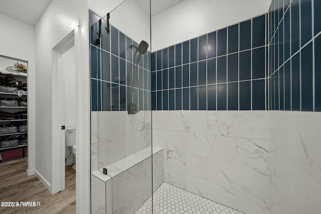 bathroom with tiled shower, hardwood / wood-style floors, and toilet