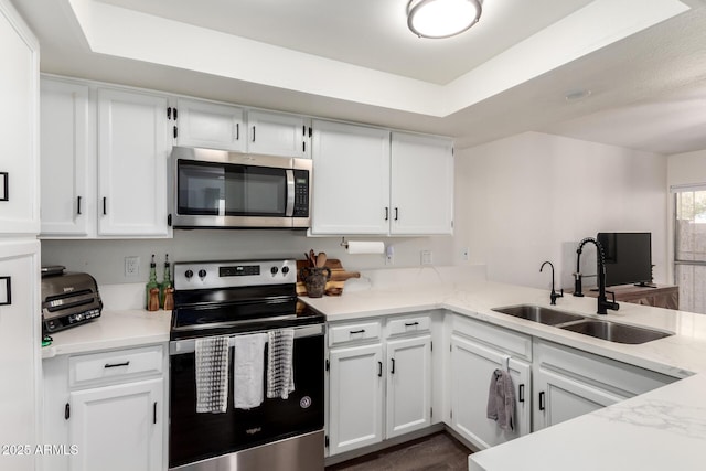 kitchen featuring white cabinets, a raised ceiling, a sink, a peninsula, and stainless steel appliances