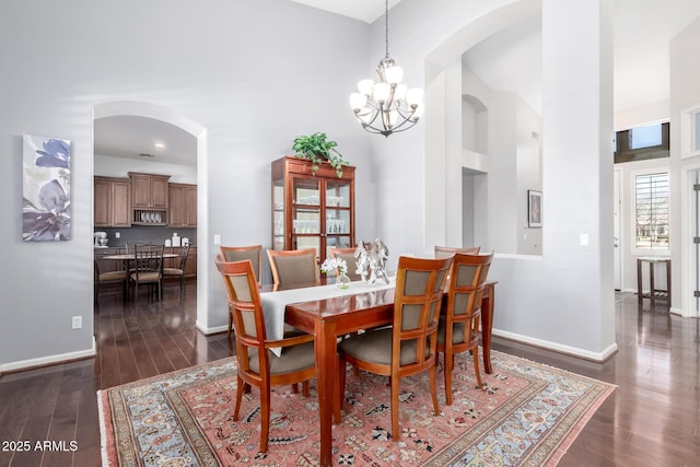 dining space featuring a towering ceiling, a chandelier, and dark hardwood / wood-style flooring