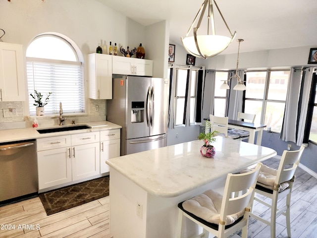 kitchen featuring sink, white cabinets, hanging light fixtures, a kitchen island, and appliances with stainless steel finishes