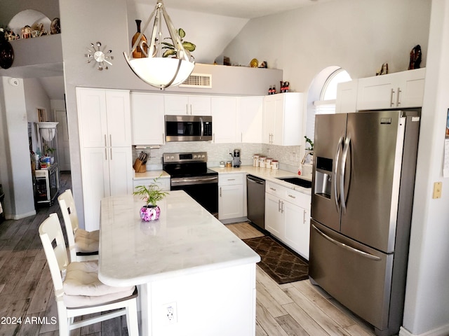 kitchen featuring white cabinetry, a breakfast bar area, stainless steel appliances, a center island, and light hardwood / wood-style flooring