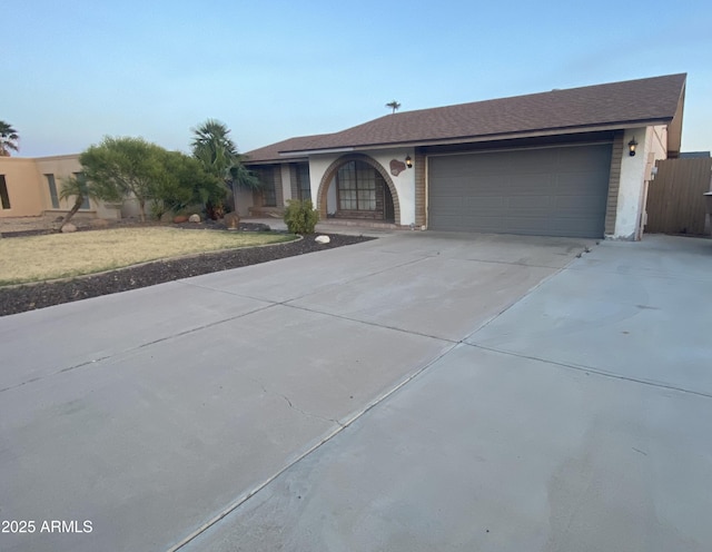 ranch-style home with an attached garage, driveway, stucco siding, and fence