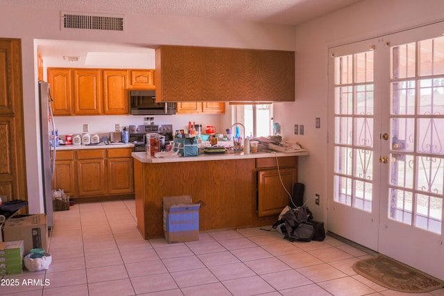 kitchen with light countertops, visible vents, light tile patterned flooring, a peninsula, and appliances with stainless steel finishes
