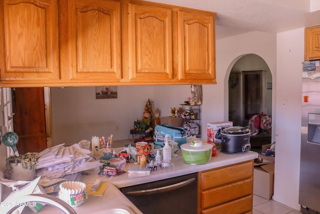 kitchen with light countertops, arched walkways, stainless steel fridge, dishwasher, and light tile patterned floors