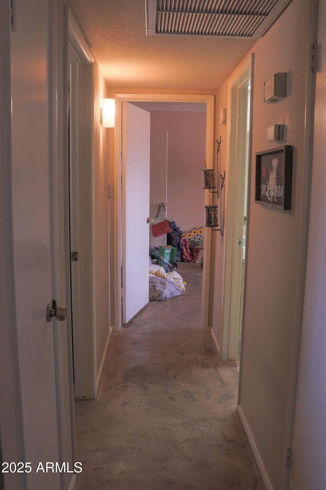hallway featuring concrete flooring, visible vents, and baseboards