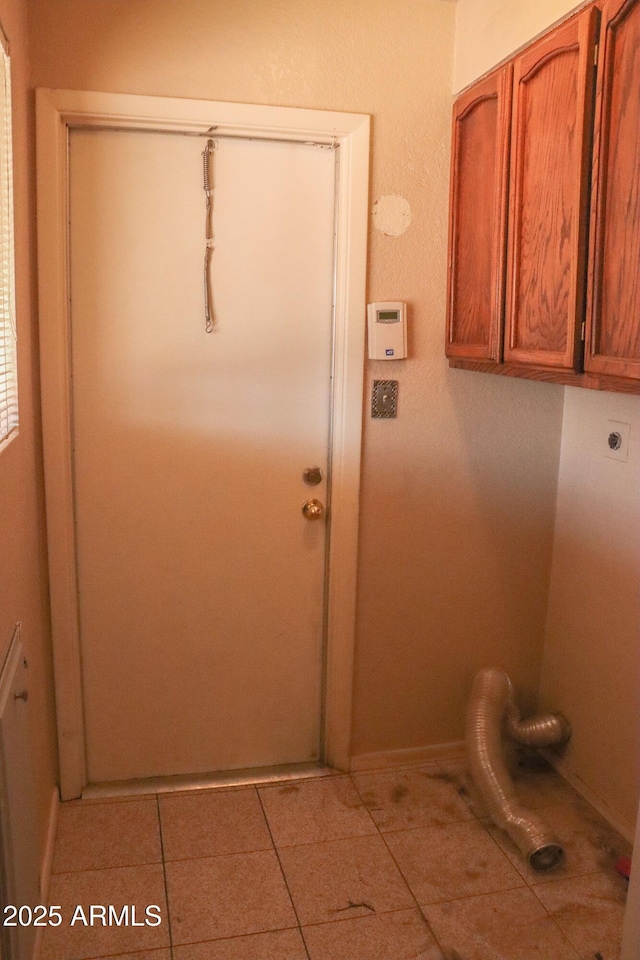 clothes washing area with baseboards, electric dryer hookup, cabinet space, and light tile patterned floors