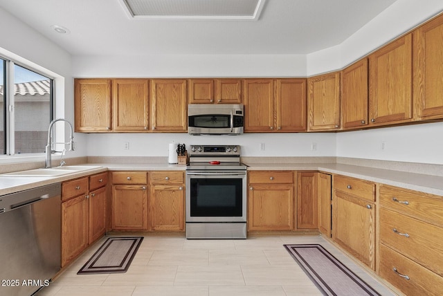 kitchen with brown cabinetry, a sink, light countertops, stainless steel appliances, and light tile patterned flooring