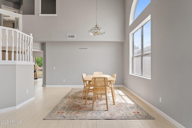 dining area with baseboards, a high ceiling, light wood-style flooring, and visible vents