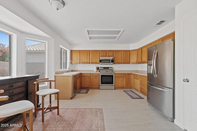 kitchen with brown cabinetry, visible vents, a sink, light countertops, and stainless steel appliances