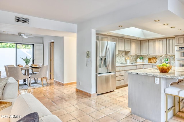 kitchen featuring light stone countertops, decorative backsplash, stainless steel fridge with ice dispenser, light tile patterned flooring, and cream cabinetry