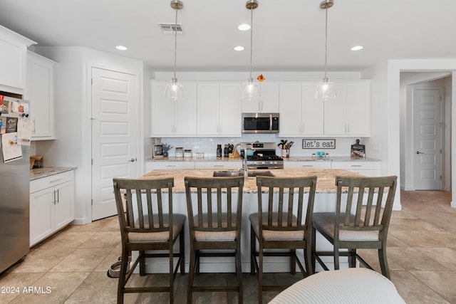 kitchen featuring stainless steel appliances, a kitchen island with sink, pendant lighting, and white cabinets