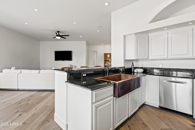 kitchen featuring a sink, dark stone countertops, stainless steel dishwasher, a peninsula, and white cabinets